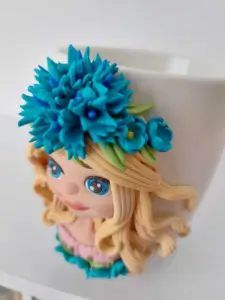 Cană handmade decorată cu figurină de fată blondă și floare albastră, design floral artistic eva art